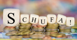 Man sieht Würfel, die zu dem Wort Schufa aufgestellt sind aud Münzen gestellt