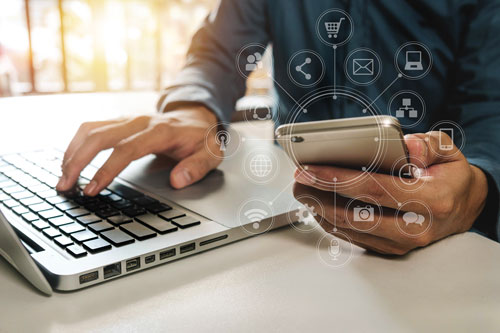 Beitragsbild zeigt Person, die einen Laptop und ein Smartphone bedient, wobei als Overlay eine transparente Mindmap von Symbolen auf Online-Banking hinweist