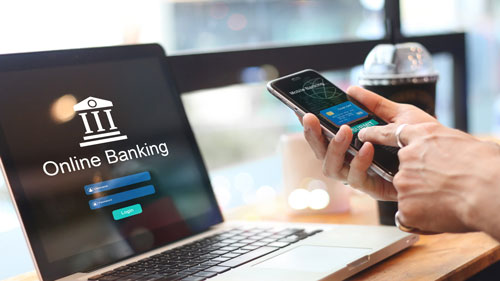 Beitragsbild zeigt Laptop mit Online-Banking-Login und eine Hand, die ein Smartphone bedient